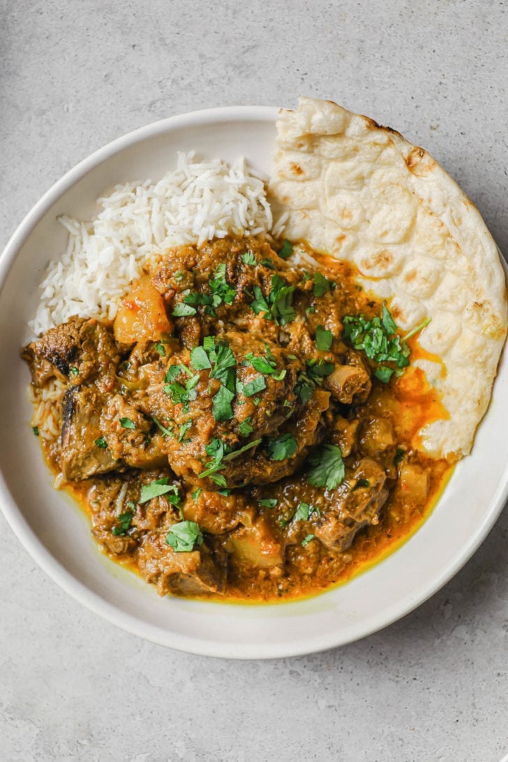 Aloo Gosht in a plate with rice and naan. 