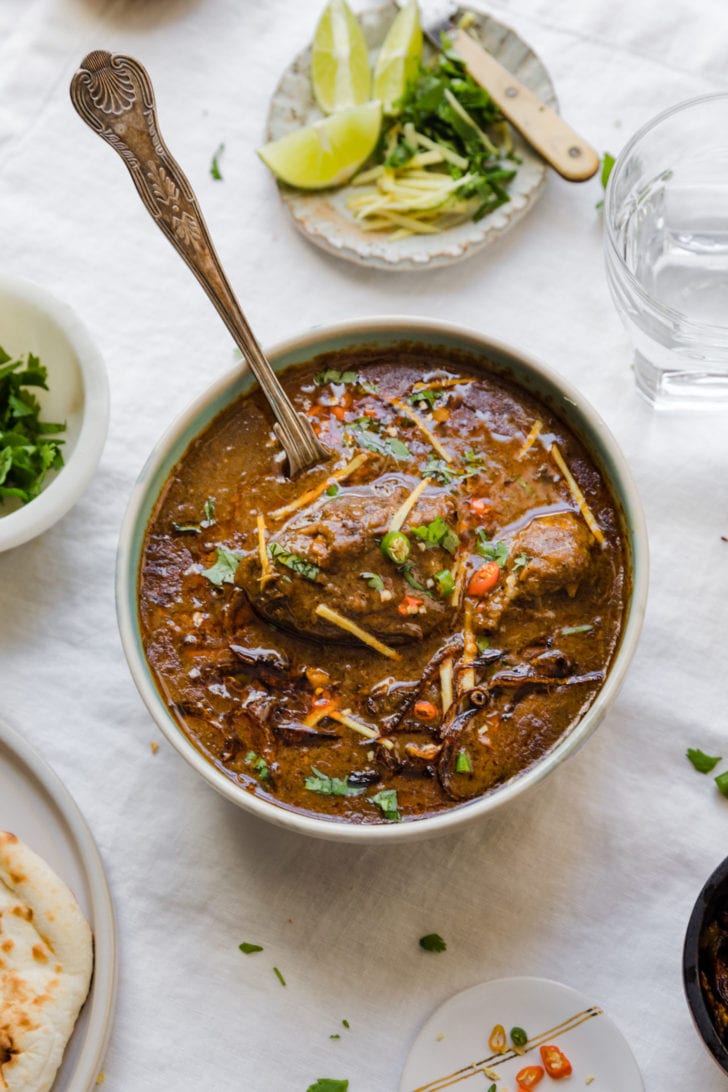 Nihari in a bowl with lemons, julienned ginger, and cilantro on the side