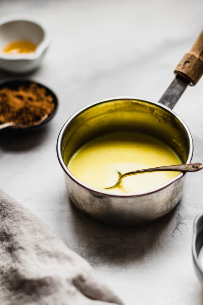 A pot of Authentic Turmeric Milk with a metal spoon in it.
