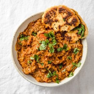 Baingan Bharta (Oven-Roasted Eggplant Curry) in a speckled bowl with naan and garnished cilantro.