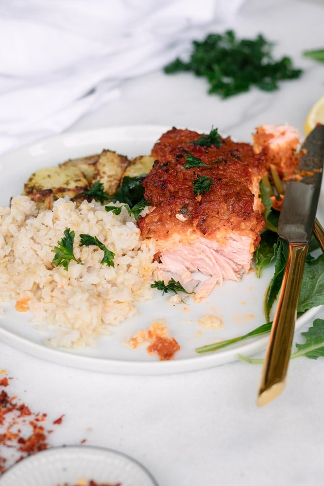 Partially eaten Spicy Baked Salmon topped with Tomato Masala on a white plate with rice and potatoes.