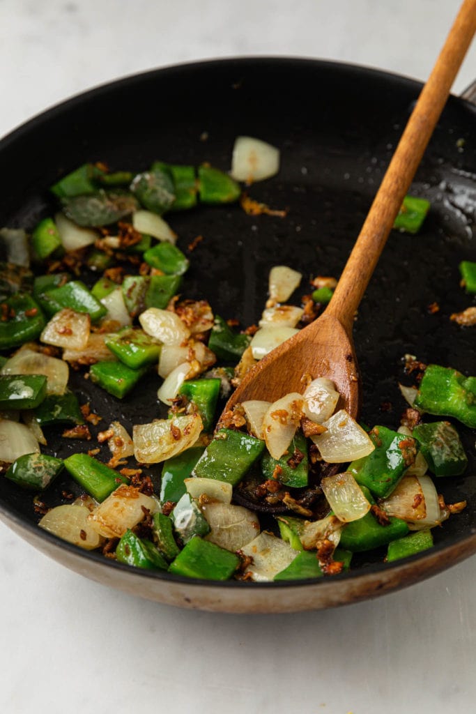 Bell peppers and onions in a skillet with a wooden spoon