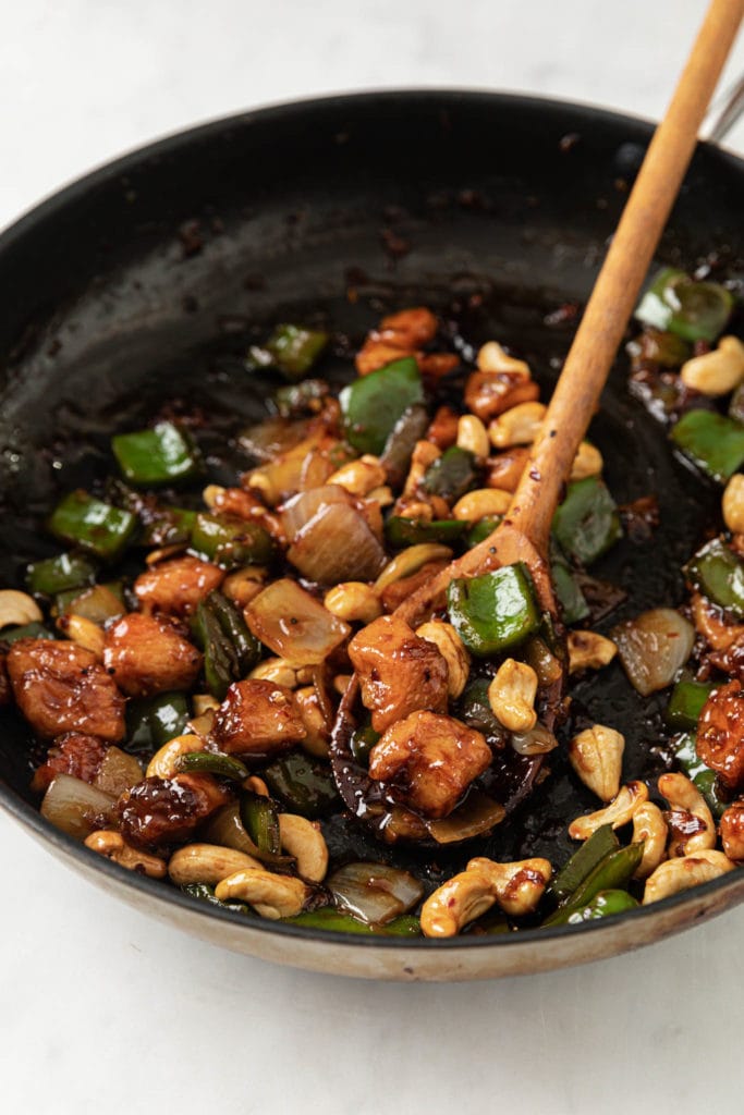cooked cashew chicken in a skillet with a wooden spoon