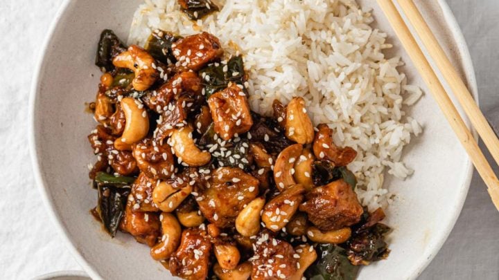 Spicy Cashew Chicken in a bowl with rice with chopsticks and sesame seeds on the side