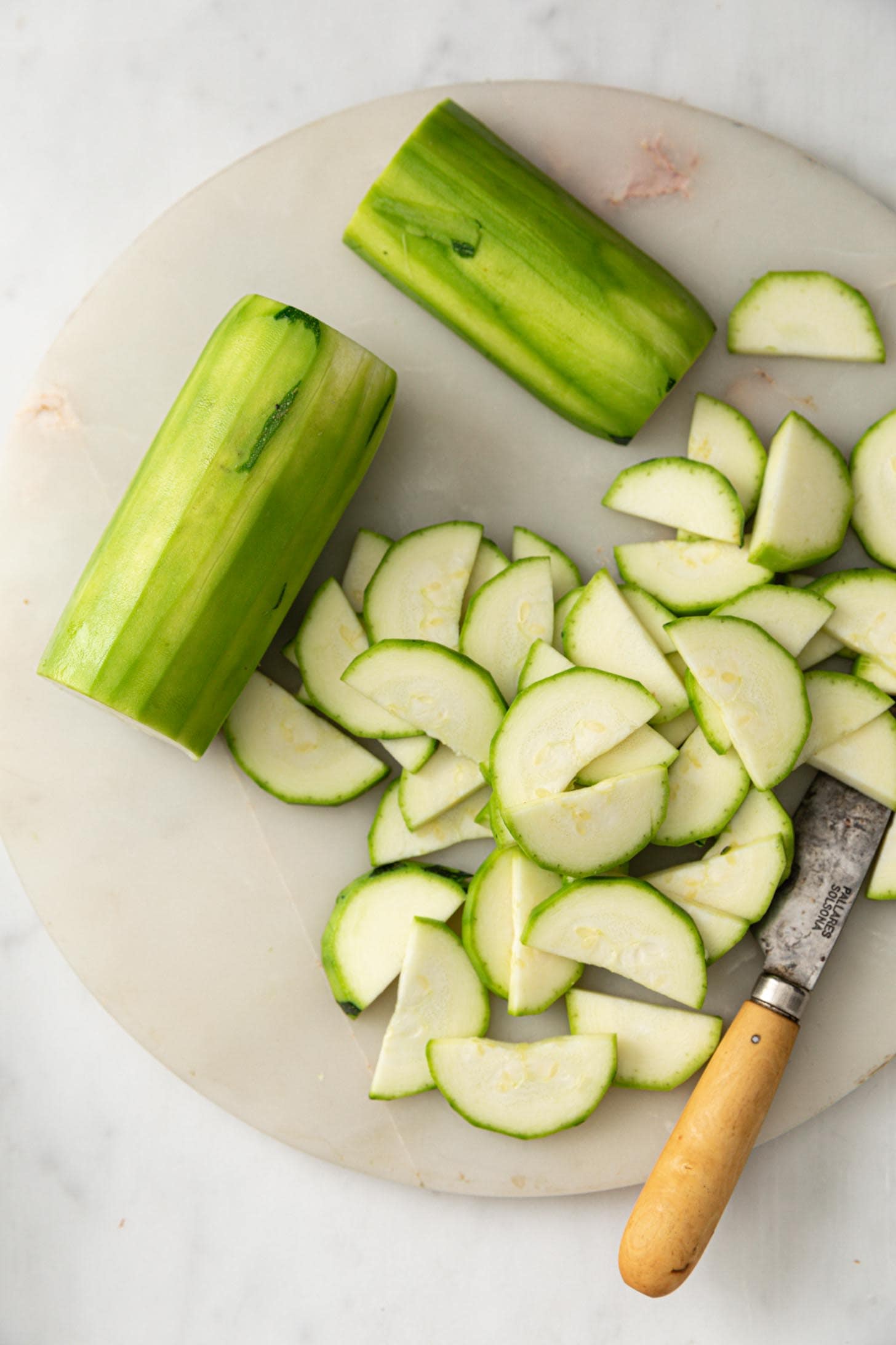 Peeled and sliced zucchini half moons on a plate with a knife.