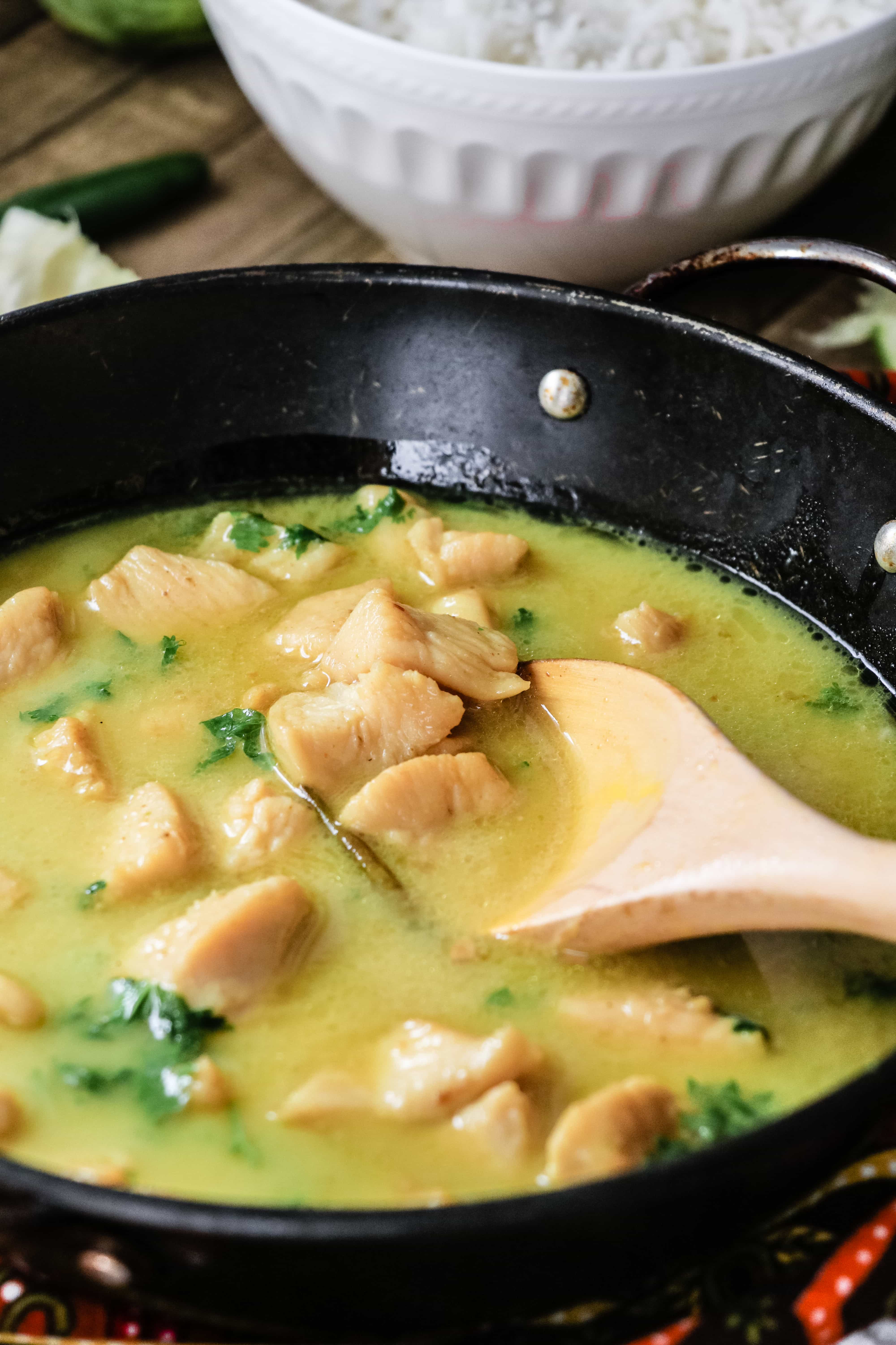 Close up of Coconut Lime Chicken Curry in a skillet with a wooden spoon.