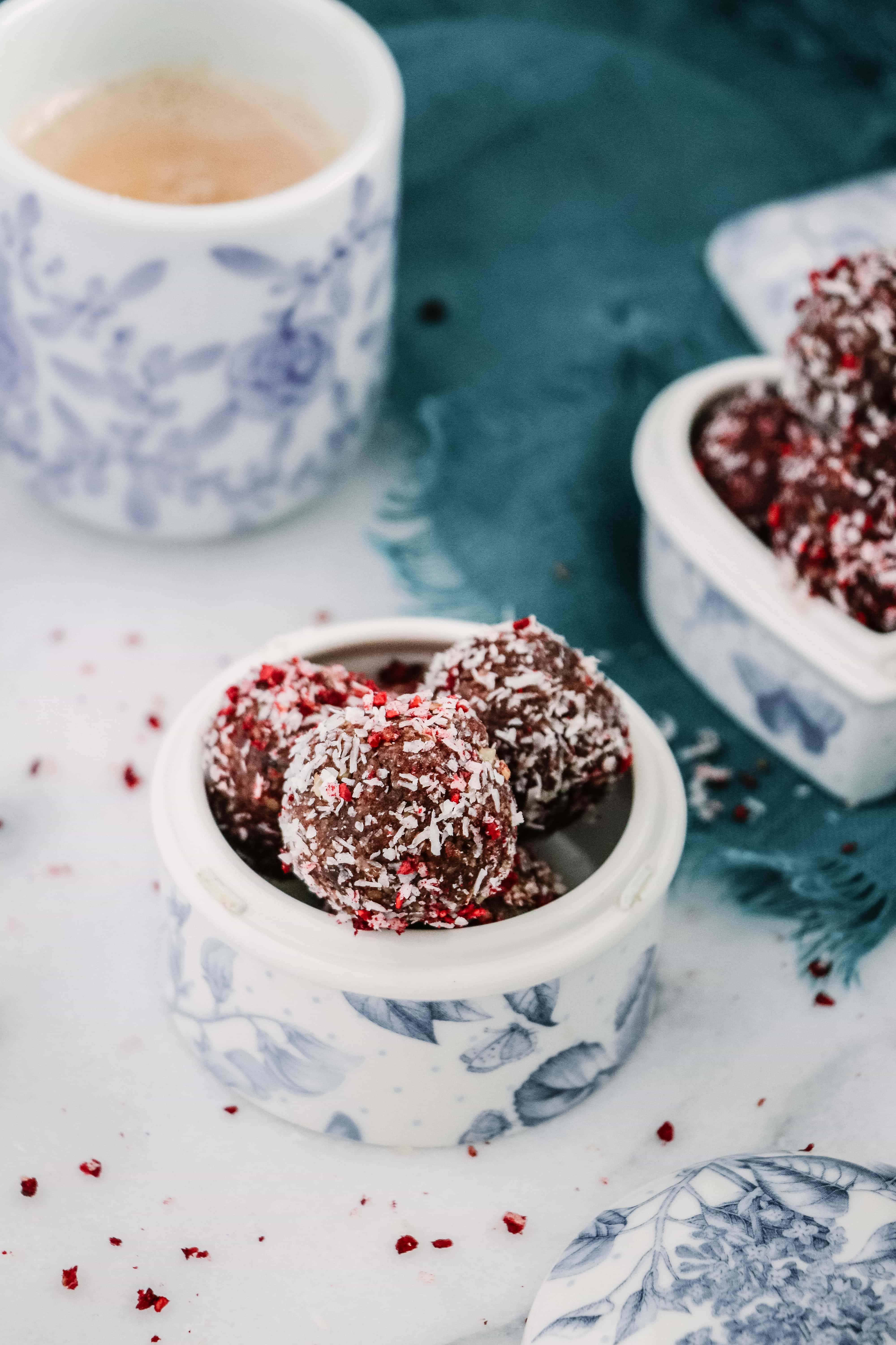 Coconut Raspberry Cacao Bliss Balls in a white round glass container.