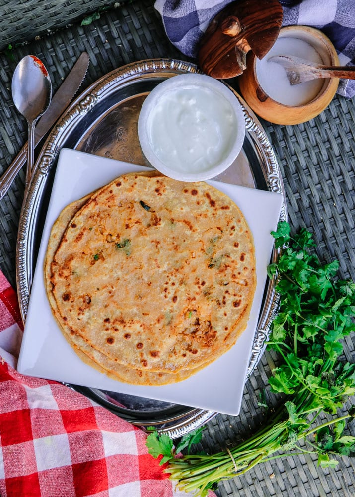 A tray with cooked parathas on a plate next to a bowl of yogurt