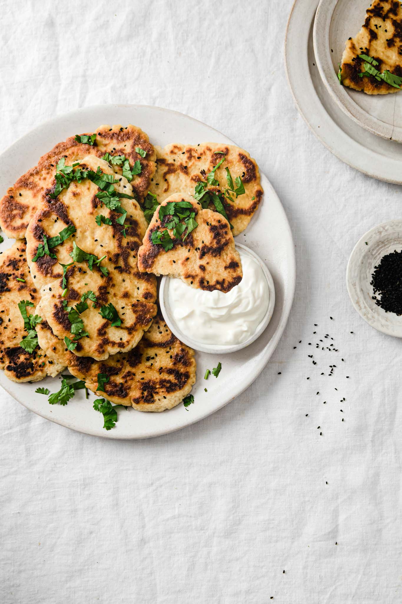 Gluten-Free Naan Bread on a white platter with cilantro sprinkled on top and a piece of naan dipped into yogurt