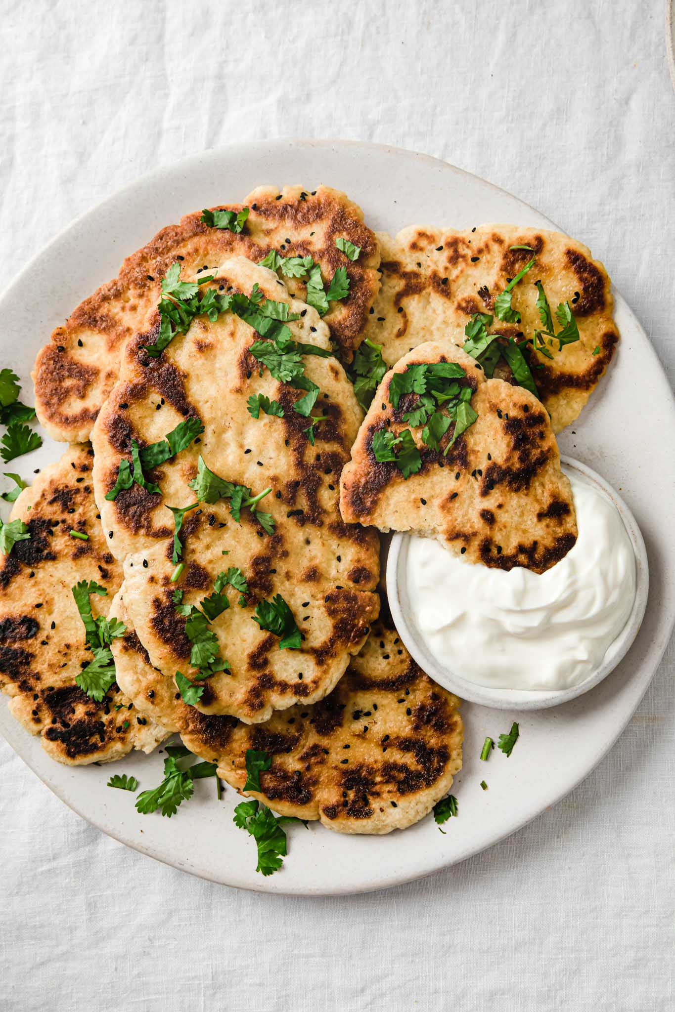 Closeup of Gluten-Free Naan on a platter and a piece of naan dipped into a bowl of yogurt 