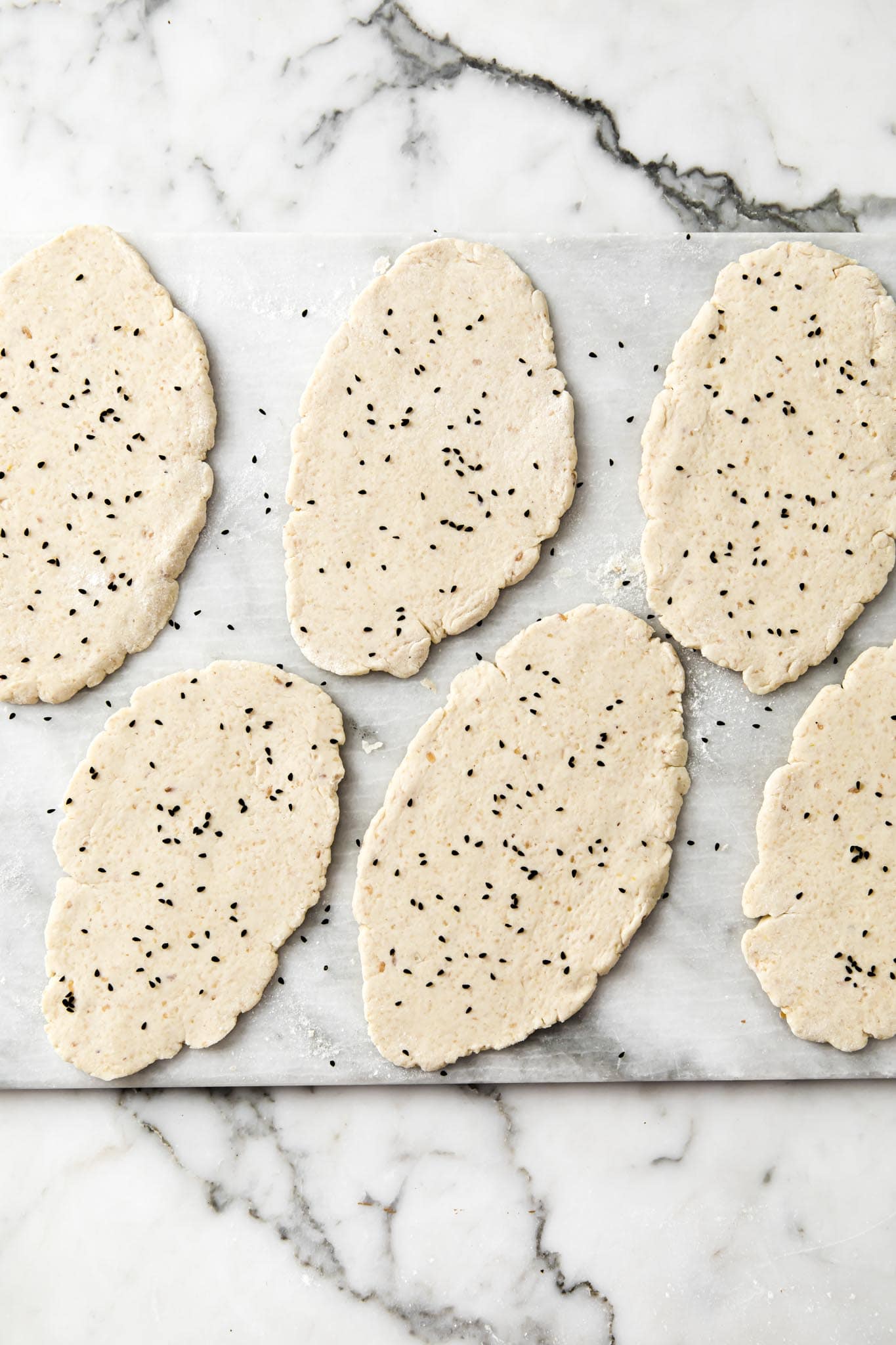 Rolled out Gluten-free naan sprinkled with nigella seeds on a marbled surface