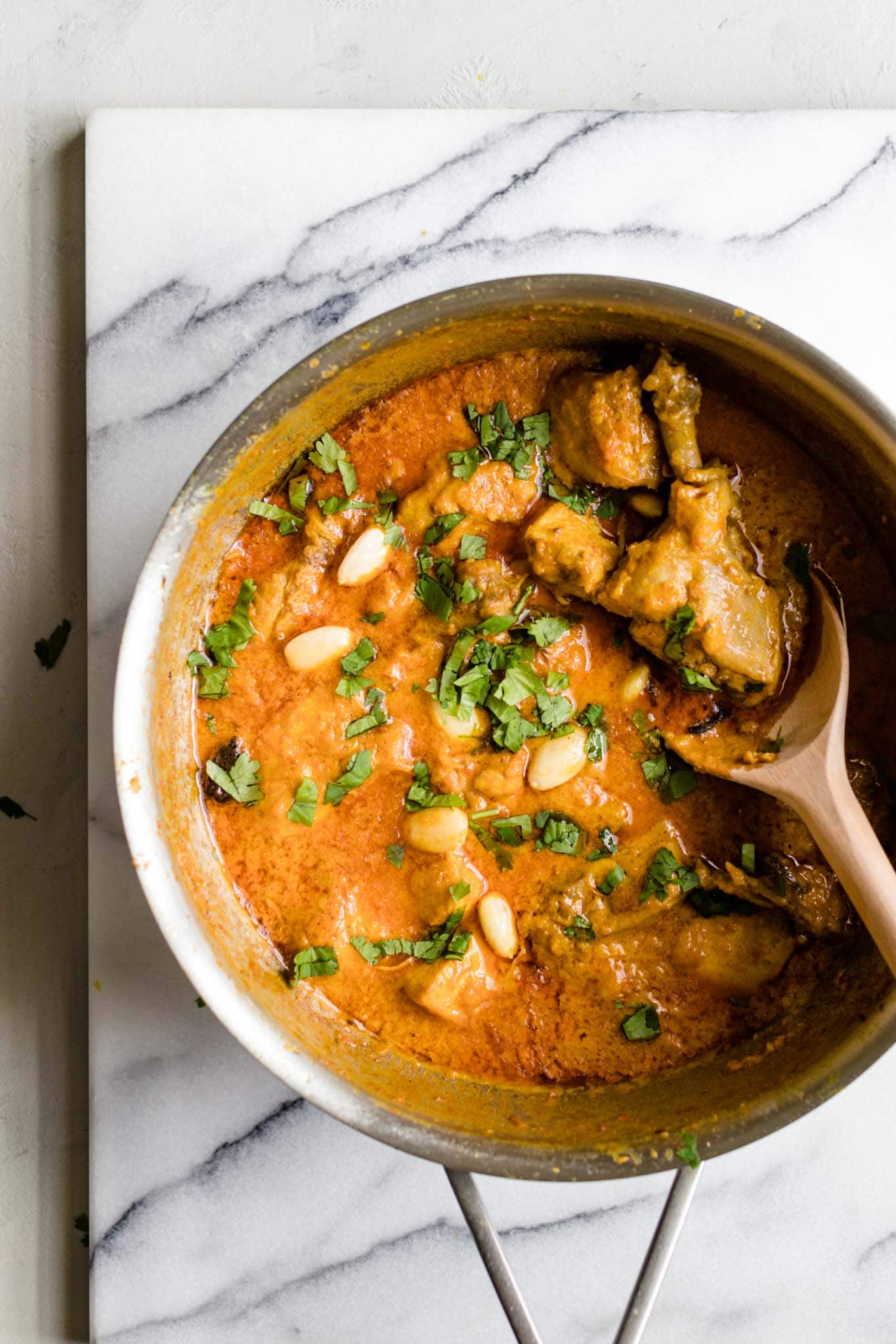 Chicken Korma garnished with almonds and cilantro in a pan with a wooden spoon