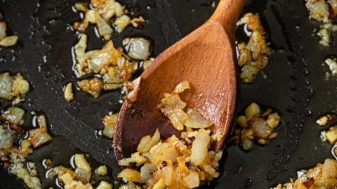 Sauteed onions with garlic and ginger in a black pan with a wooden spoon