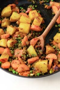 Potatoes, carrots, and peas in a black pan with a wooden spoon