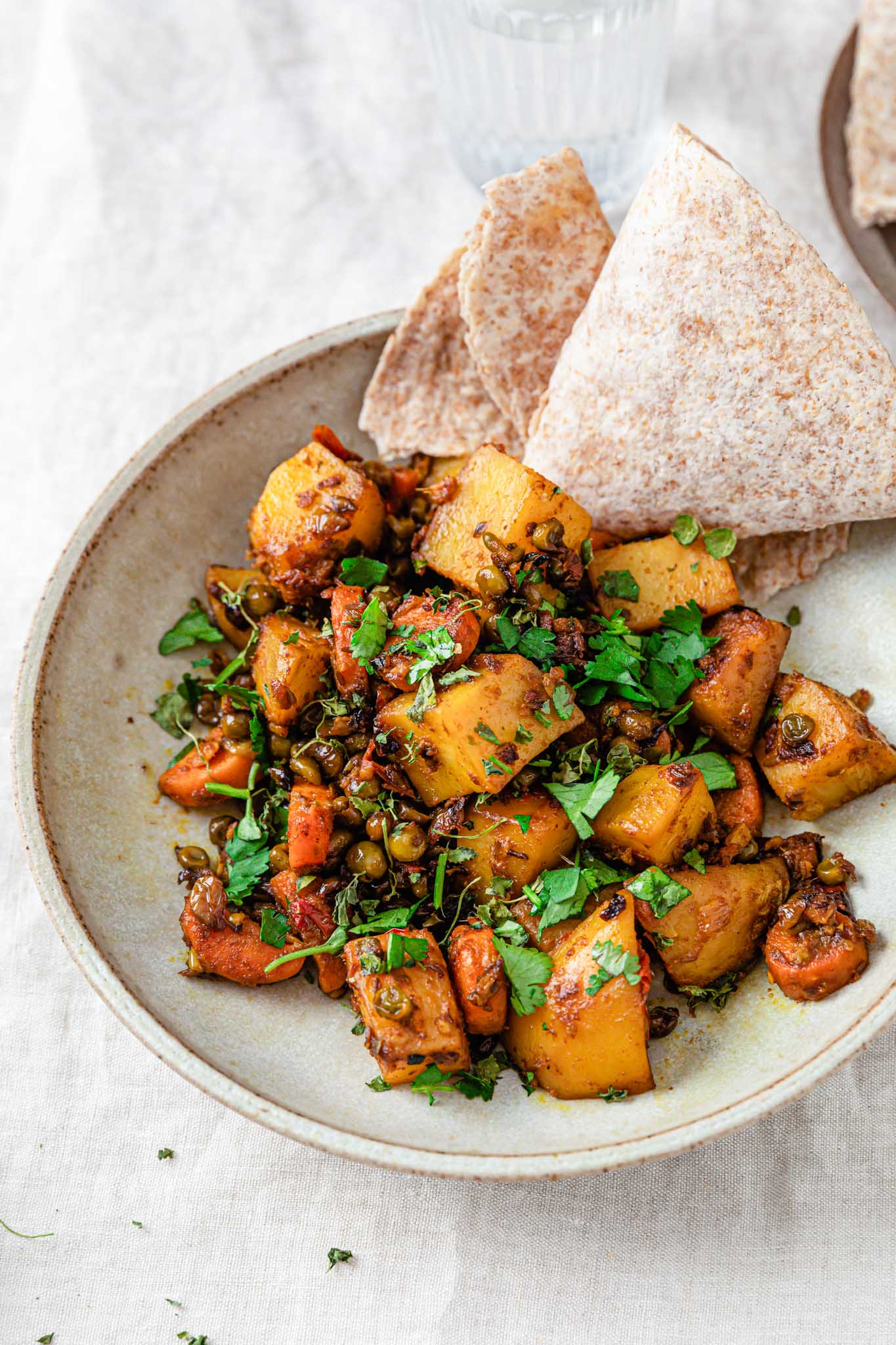 Potatoes, carrots, and in a beige bowl with a piece of roti on the side.