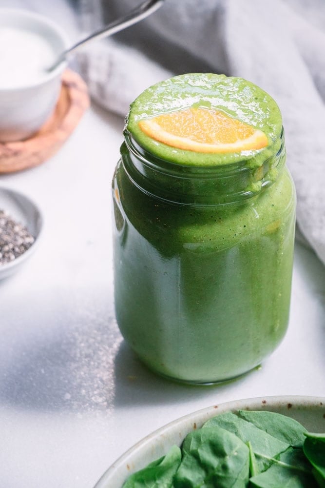 Iron Boosting Orange Green Smoothie in a glass mason jar topped with a slice of orange.