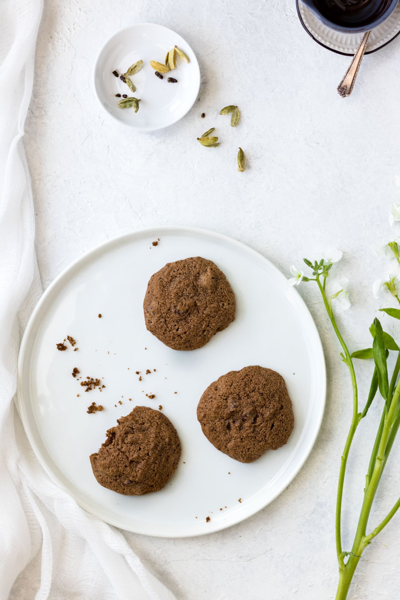 Three Gluten-Free Double Chocolate Cardamom Cookies on a white plate with some crumbs.