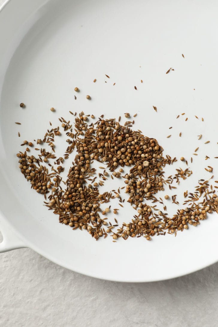 Toasted coriander and cumin seeds on a white skillet