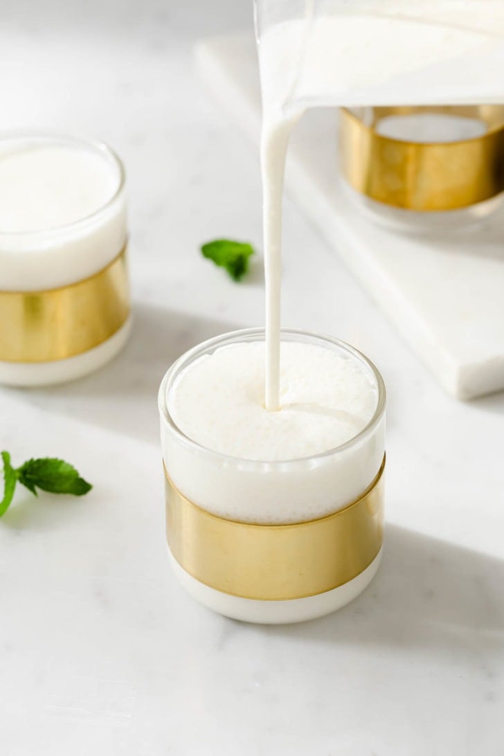 Pouring frothy sweet lassi into a glass.