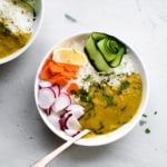 A white bowl filled with Instant Pot Red Lentil Dal, Basmati rice, ribbon of cucumber, sliced carrots and radishes and a lemon wedge.