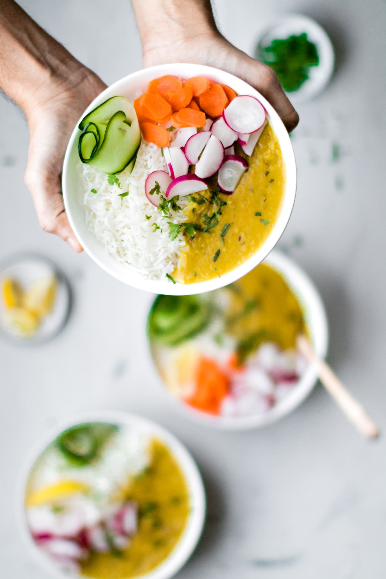 Holding a white bowl of Instant Pot Red Lentils, Basmati rice, ribbon of cucumber, sliced carrots and radishes.