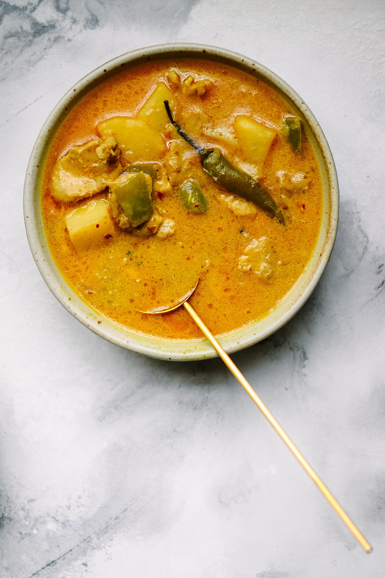 A bowl of Coconut Chicken Curry with Potatoes with a golden spoon.