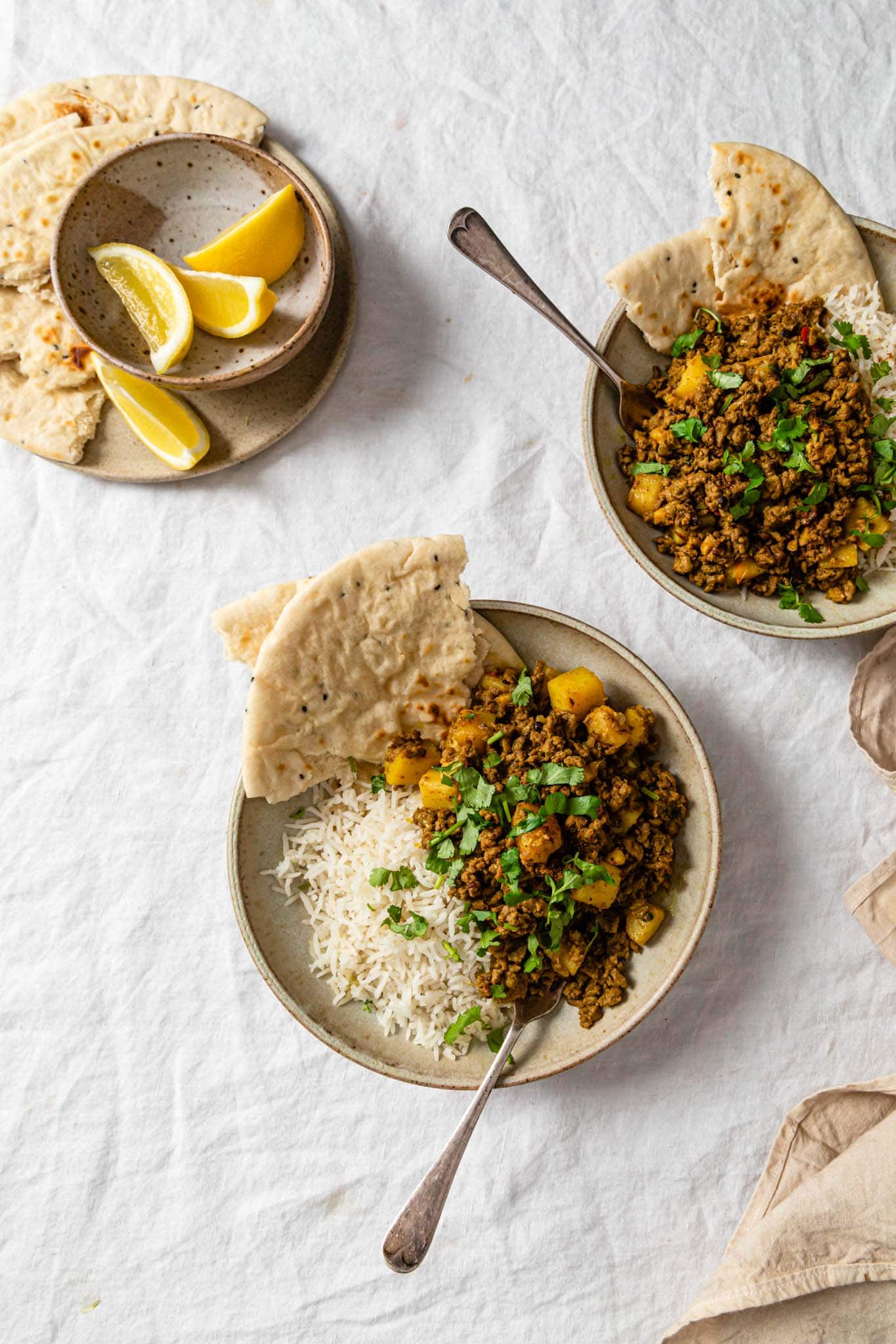 Bowls with Aloo Keema served with naan, rice, and lemon wedges