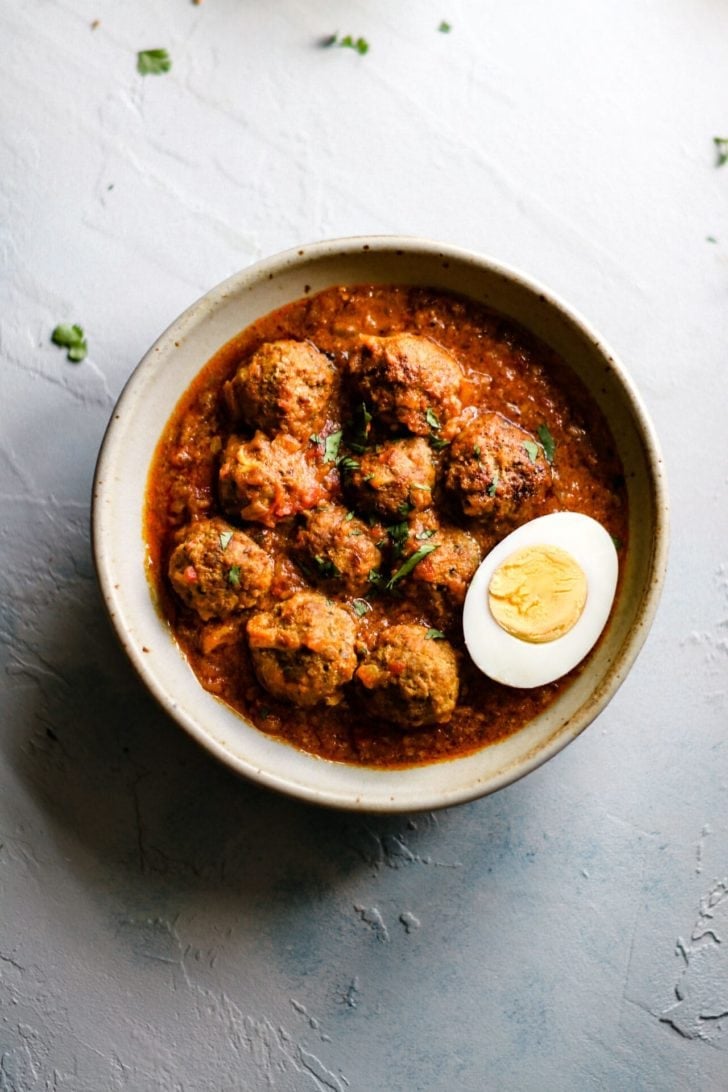 A bowl of Pakistani Beef Kofta Curry garnished with half a hard boiled egg and cilantro.