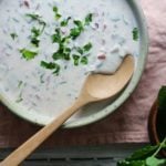 Cucumber Raita in a bowl with a wooden spoon and cilantro sprinkled on top