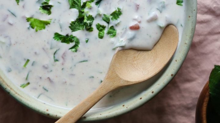 Cucumber Raita in a bowl with a wooden spoon and cilantro sprinkled on top