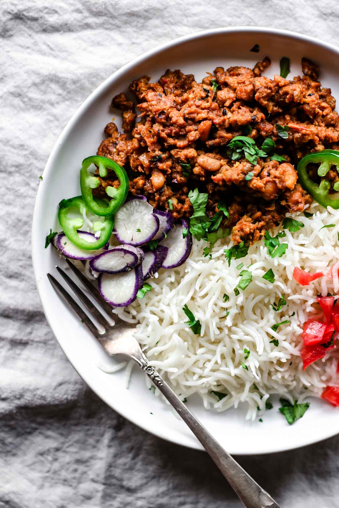 Top view of Keema Lobia on a white plate with a silver fork with rice and vegetables.