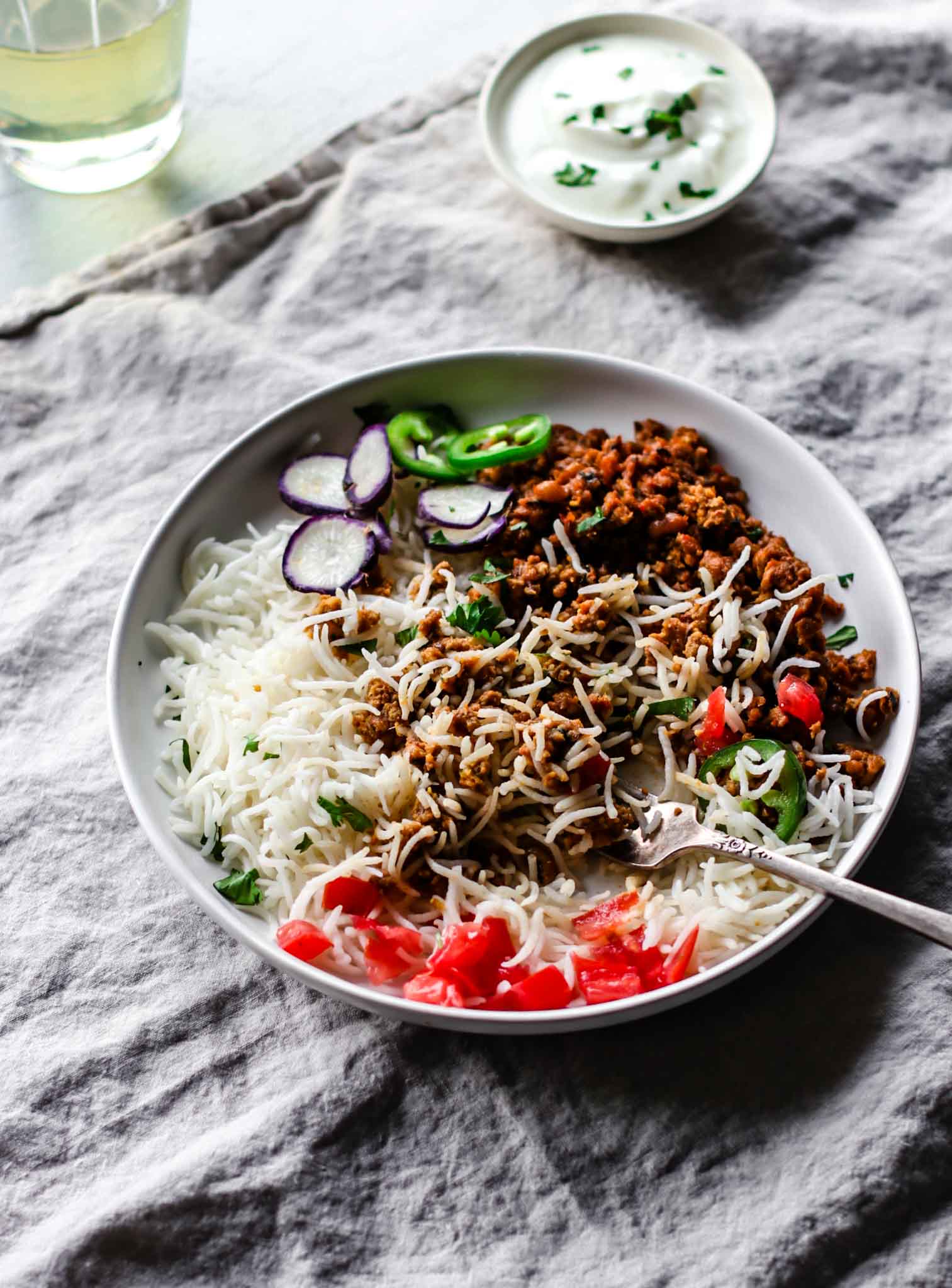 Keema Lobia mixed with rice on a white plate with a silver fork, vegetables, and yogurt on the side