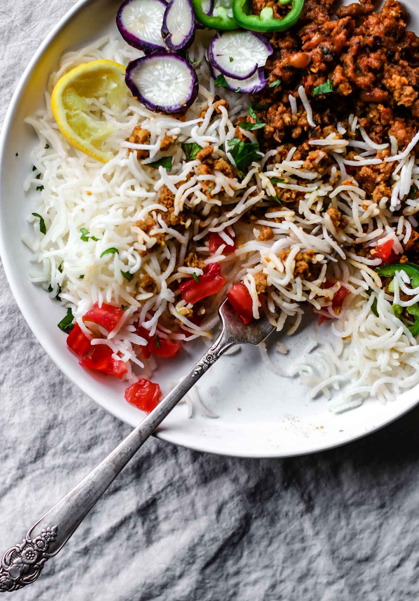Close up of a plate of Keema Lobia mixed with rice with a silver fork and vegetables.