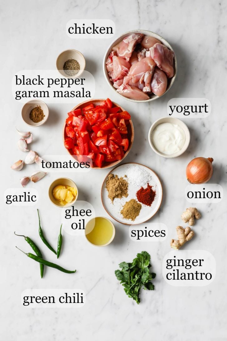 Ingredients for Chicken Karahi such as tomatoes, garlic, ginger, onion, and spices placed on a marbled surface