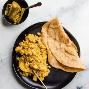 Scrambled Egg and Potatoes and paratha on a black plate with a gold spoon
