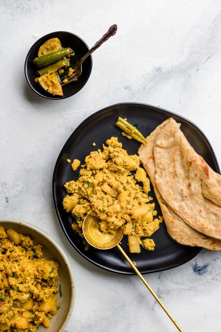 Scrambled Egg and Potatoes and paratha on a black plate with a gold spoon