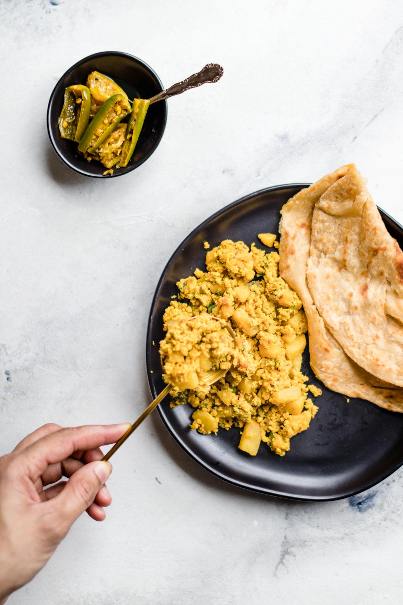 Holding a spoon with scrambled egg and potato curry over a plate