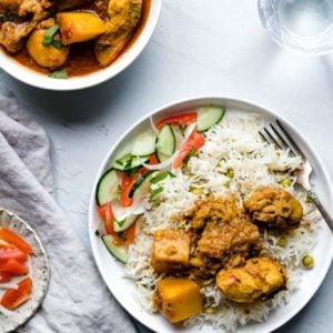 Chicken Curry with potatoes on a plate with rice and vegetables with a glass of water on the side