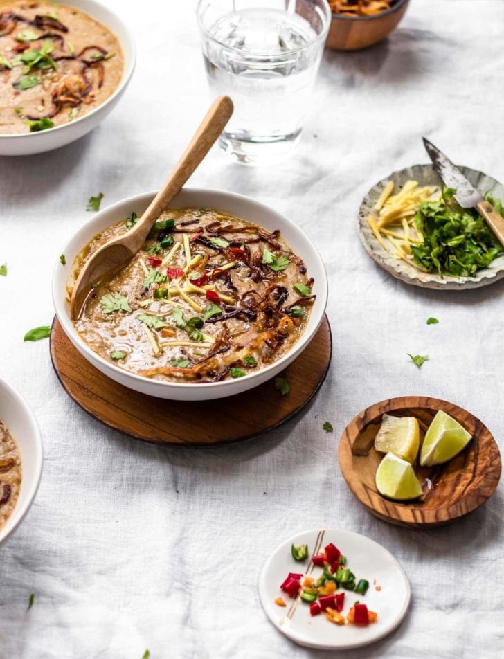Instant Pot Pakistani-style Haleem made with beef and grains in a white bowl with wooden spoon and garnishing 