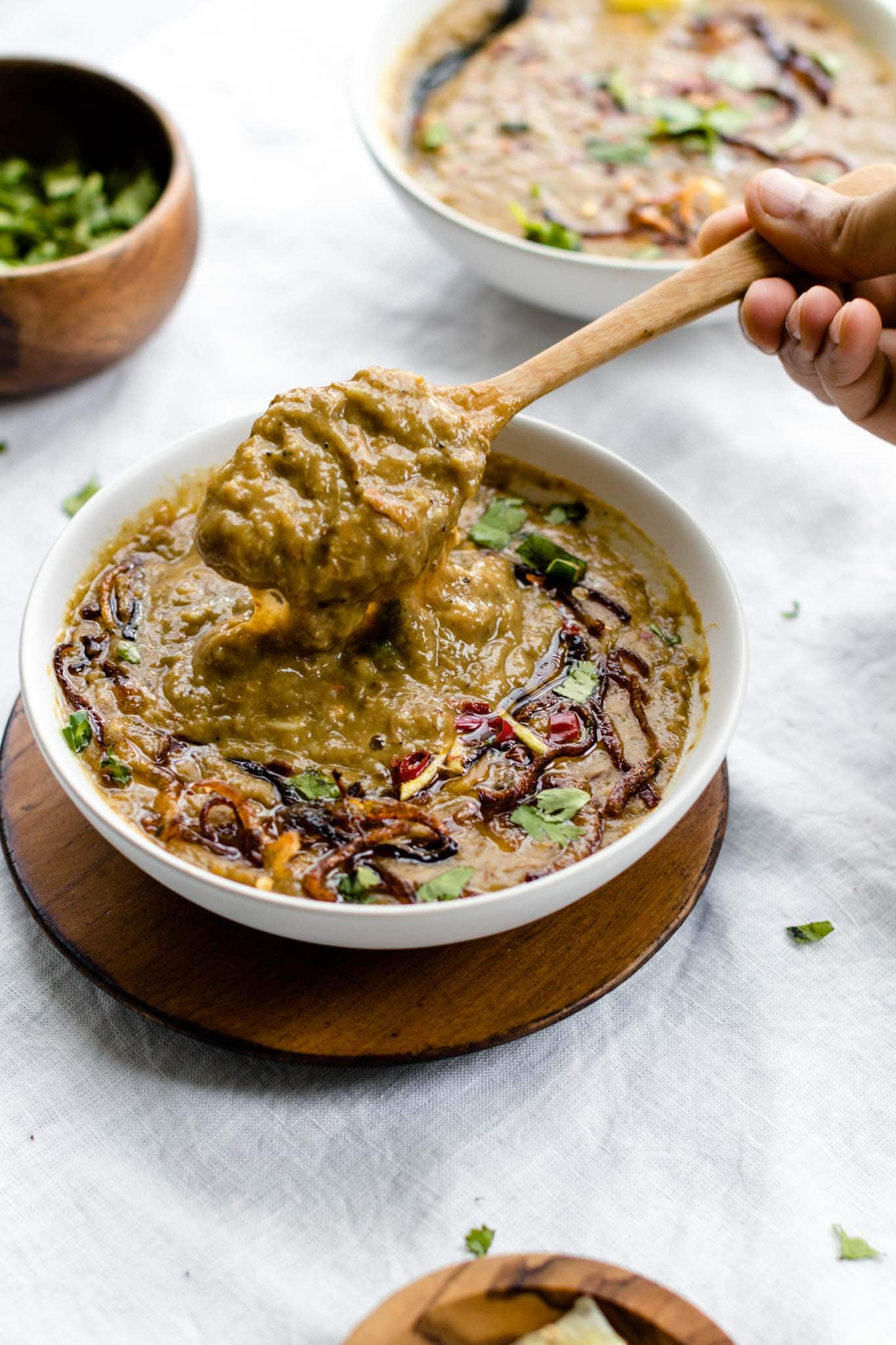 Scooping Haleem with a wooden spoon from a white bowl