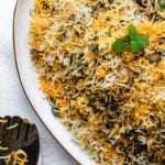 Chicken Biryani on a gold-trimmed platter with a silver rice spoon resting on the side