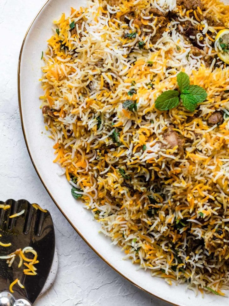 Chicken Biryani on a gold-trimmed platter with a silver rice spoon resting on the side