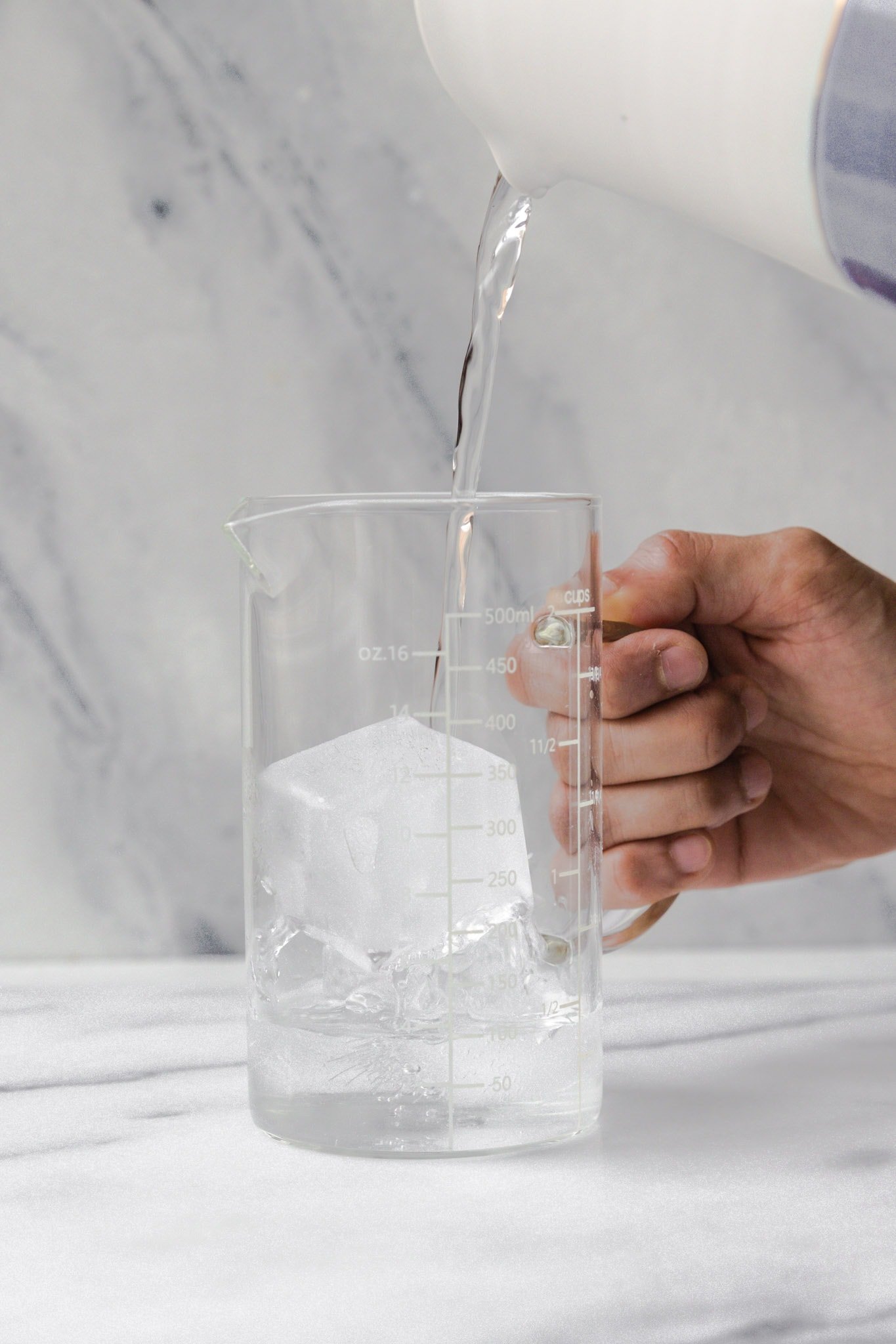 Water being poured into a measuring cup with ice cubes to prepare ice water for Kashmiri Chai