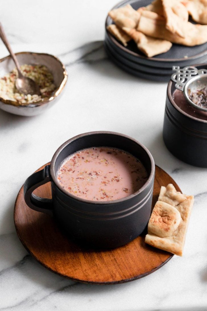 Dark cups filled with pink Kashmiri Chai garnished with nuts and served with a broken piece of naan