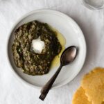 Sarson Ka Saag with a dollop of butter on a plate with spoons and makai ki roti on the side