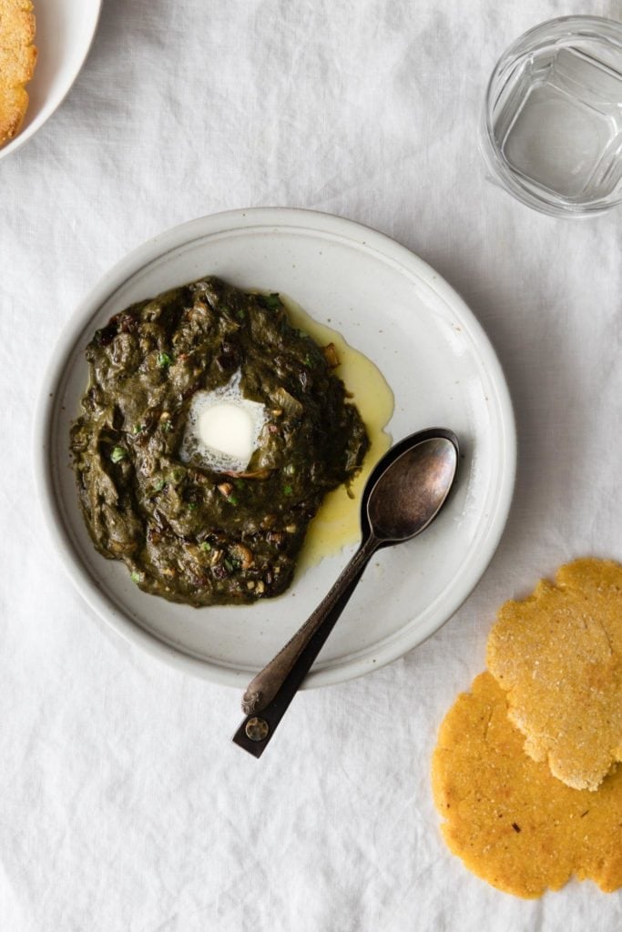Sarson Ka Saag with a dollop of butter on a plate with spoons and makai ki roti on the side