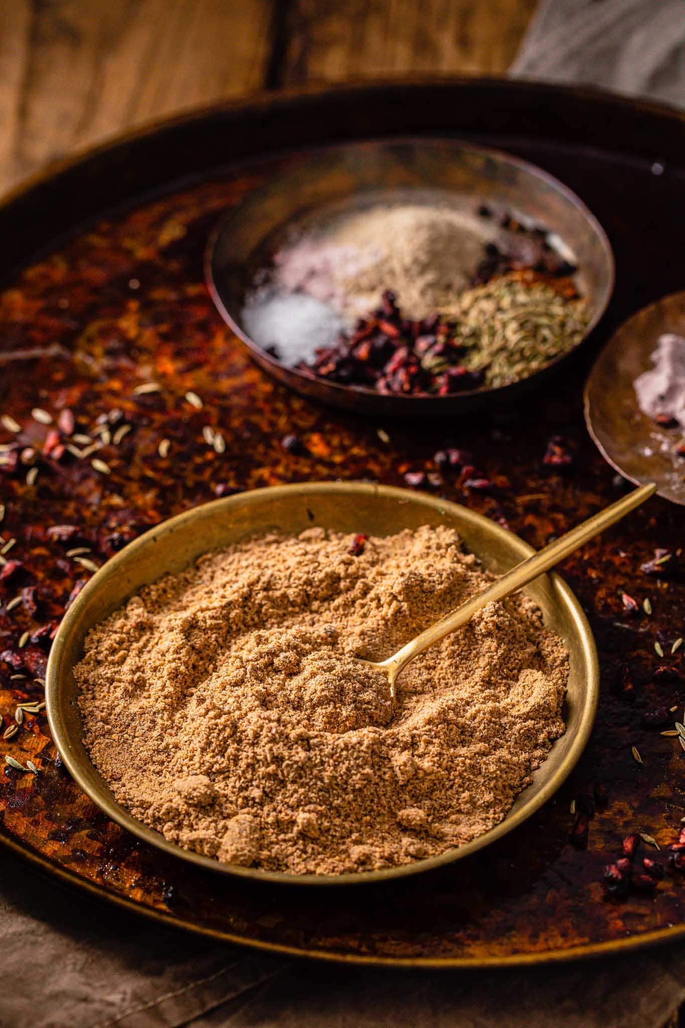 Chaat Masala powder in a gold bowl with a small golden spoon with spices in the background