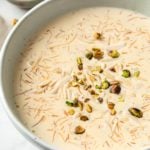A large bowl with sheer khurma served with spoons and nuts in small bowls