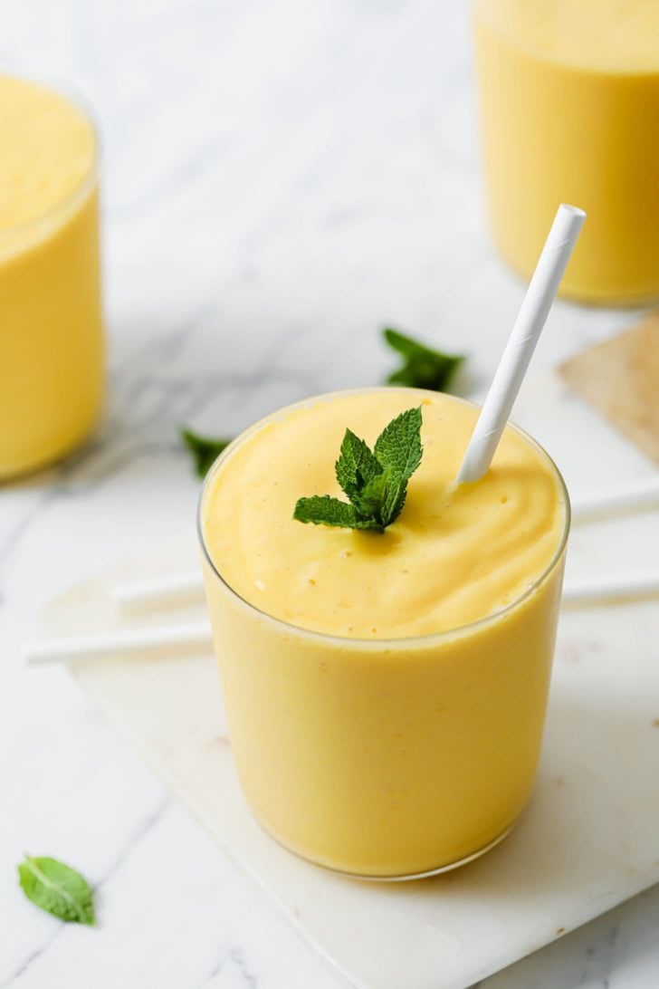 A clear glass with mango lassi garnished with mint