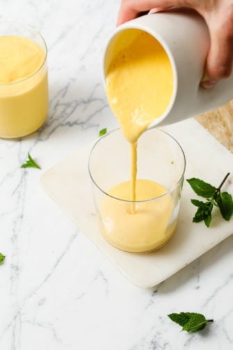 Pouring Mango Lassi from a white jug into a clear glass